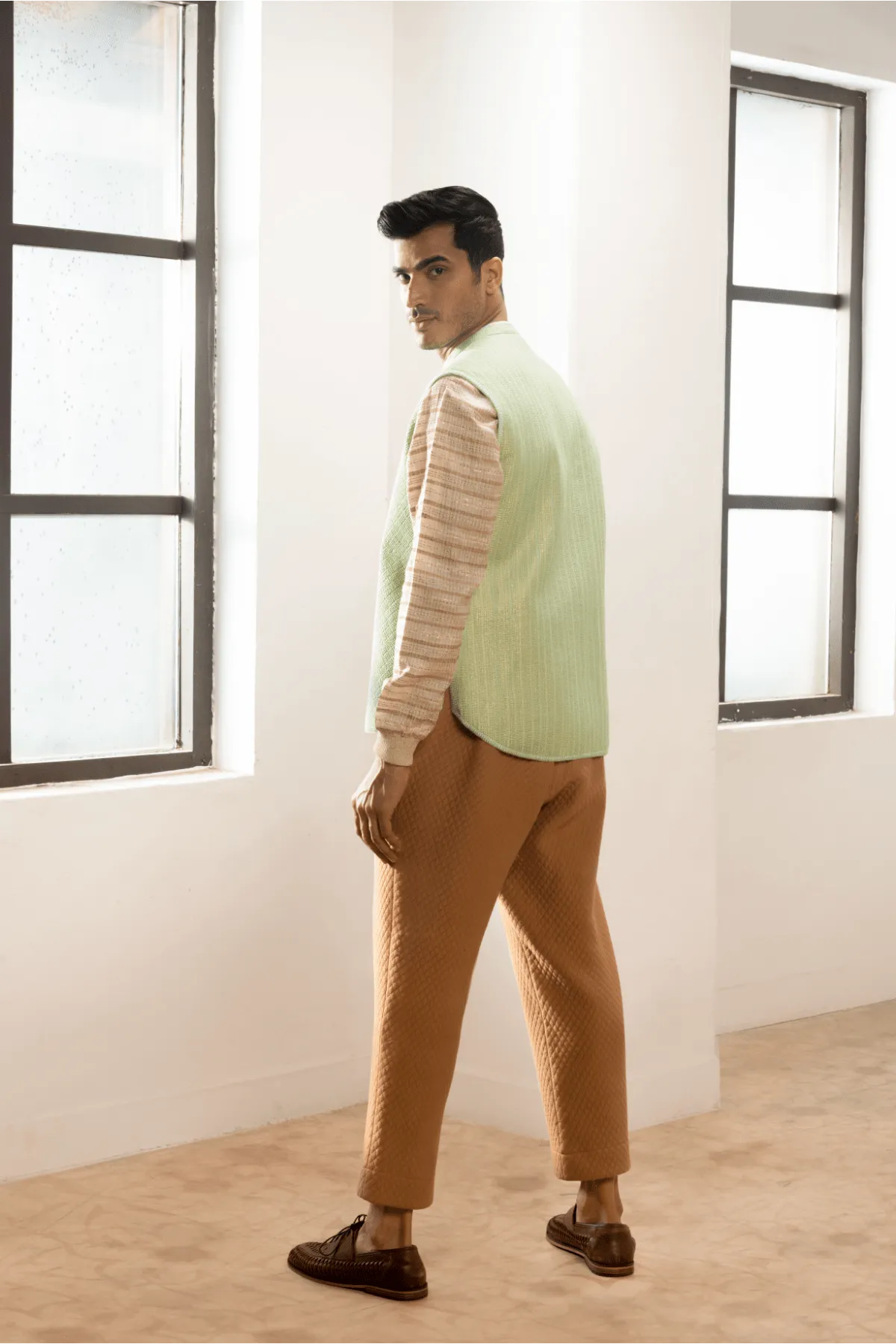 Green textured jacket with cream pullover and beige pants.