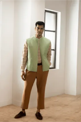 Green textured jacket with cream pullover and beige pants.